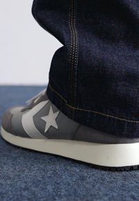Sive teniske z belimi poudarki, z zvezdastim logotipom in teksturirano površino. Uparjene s temnimi jeans hlačami z kontrastnimi šivi.