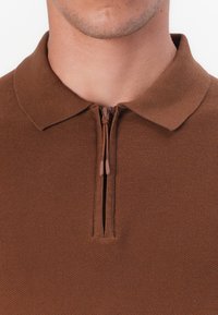 Polo castanho com fecho éclair, com um acabamento texturizado, apresentando um colarinho e um pequeno fecho à frente.