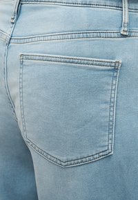 Κοντινό πλάνο τζιν παντελονιού ανοιχτού μπλε χρώματος που δείχνει την πίσω δεξιά τσέπη με εμφανείς ραφές και θηλιά ζώνης.