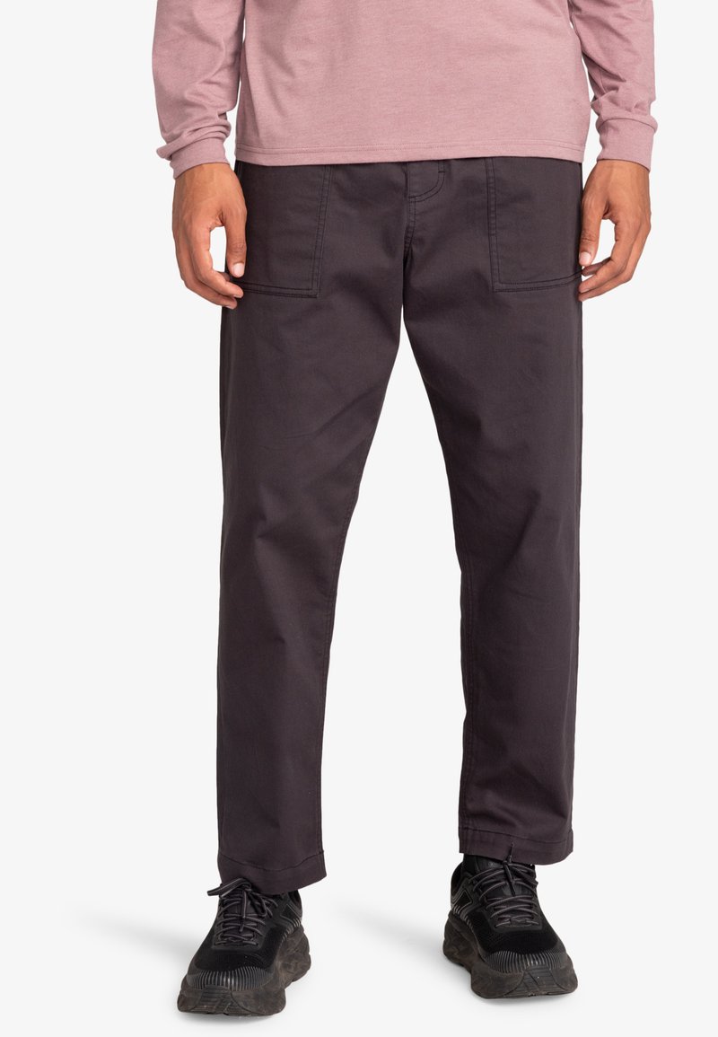 Zwarte katoenen broeken met een rechte snit, met twee voorkezen en contrasterende stiksels. Gecombineerd met een roze top met lange mouwen en donkere schoenen.