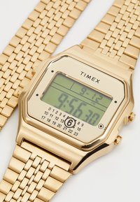 Goldfarbenes Edelstahl-Digitaluhr mit quadratischem Zifferblatt, grünem LCD-Display und strukturiertem Metallarmband. Mit Datum- und Uhrzeit-Anzeige.