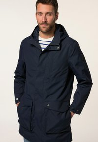 Marineblauwe waterdichte jas met capuchon, voorzien van een rits aan de voorkant, drukknoopsluiting en twee grote voorzakken. Gladde stof met minimale afwerking.