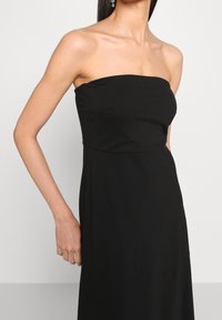 Svart axelbandslös klänning med figursydd överdel, flödande kjol, slät textur och minimalistisk design som framhäver rena linjer och en elegant silhuett.