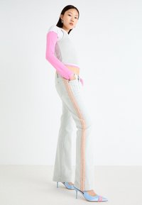 Zapatos de tacón alto azul claro, top corto gris con detalles en rosa y jeans acampanados gris claro con una franja lateral rosa y bolsillos.