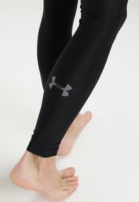 Black athletic leggings made of a smooth, stretchy material, featuring a gray logo on the left calf. Ankle-length design, fitted shape.