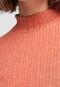 Gerippter Rollkragenpullover aus weichem, korallenfarbenem Stoff. Verfügt über einen hohen Kragen und ein strukturiertes Muster mit vertikalen Streifen für zusätzliche Tiefe.