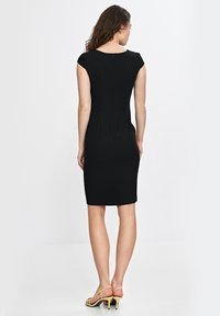 Czarna dopasowana sukienka z krótkimi rękawami, szwami księżniczki i zamkiem błyskawicznym z tyłu. Ma długość do kolan i jest zestawiona ze złotymi szpilkami na kostkę.