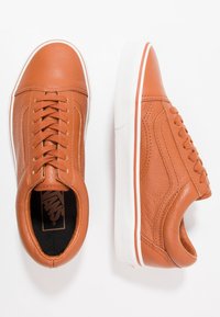 Baskets en cuir marron avec une finition texturée, des lacets plats, une semelle en caoutchouc blanche et une bande accent rouge le long des bords de la semelle.