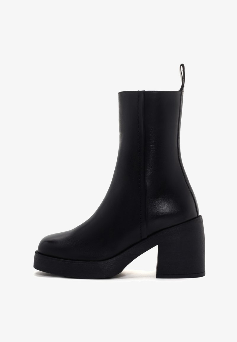 Bottine noire en cuir avec un talon épais, texture lisse et une languette à l'arrière. Design simple aux lignes épurées.