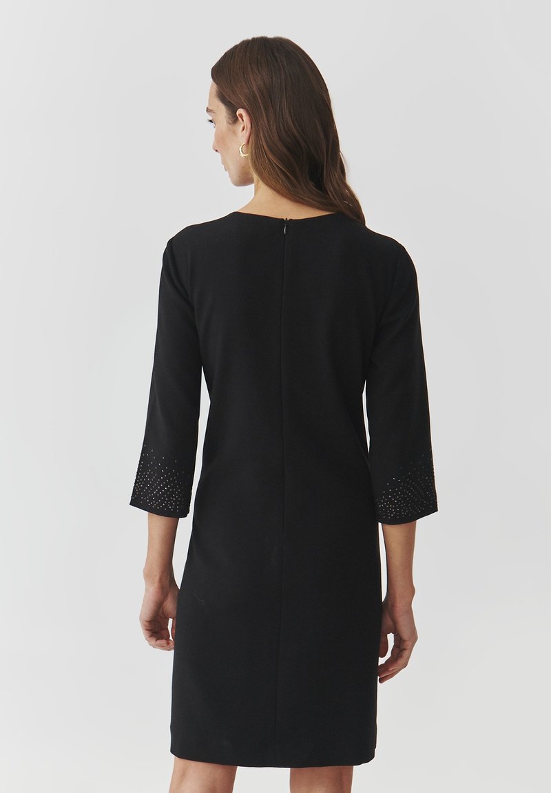 Czarna sukienka z rękawami o długości trzech ćwiartek, z teksturowanym, ćwiekowanym wzorem na mankietach oraz z zapięciem na suwak z tyłu. Gładki materiał.