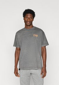 Γκρι κοντομάνικο μπλουζάκι με χαλαρή εφαρμογή και μικρή πορτοκαλί γραφική ένδειξη "City" στο στήθος. Το ύφασμα φαίνεται μαλακό και ελαφρώς υφασμένο.