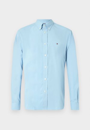 Hele sinine, nööbitav särk avara kraega, pikkade varrukatega ja väikese logoga rinnal. Valmistatud siledast kangast.