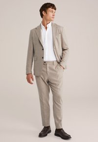 Helebež suit, mis on valmistatud tekstureeritud kangast, sisaldab ühekordset jakki, sobivaid pükse ja valget särk. Pruunid loafers lõpule viivad ilme.