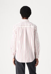 Camicia bianca con righe verticali rosse, maniche lunghe, polsini con bottoni e orlo curvo. Design del colletto semplice, tessuto leggero.