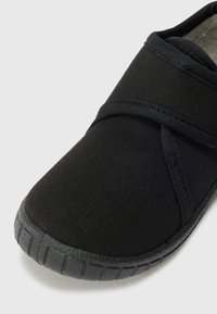 Scarpa nera in tela con design a cinturino incrociato, suola in gomma con dettagli testurizzati e rivestimento interno morbido.