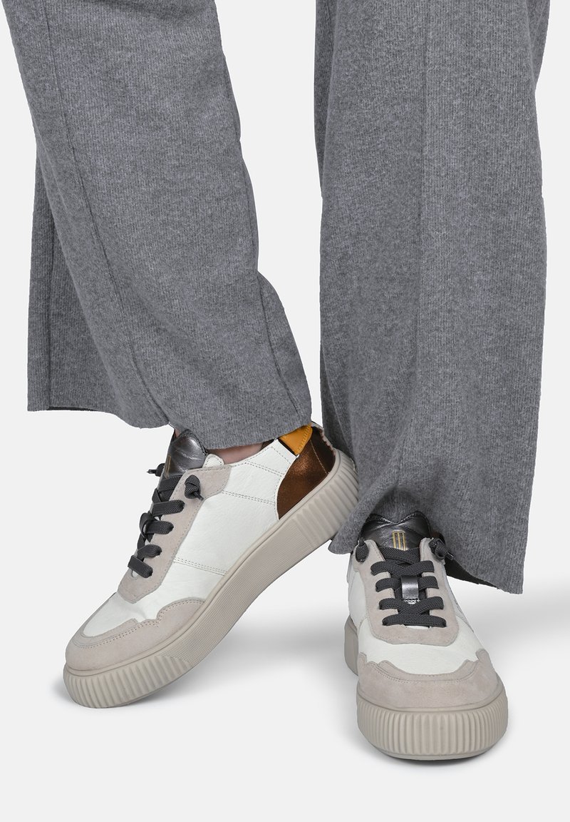 Sneakers in pelle bianchi, grigi e bronzo con dettagli testurizzati, una suola spessa e lacci. Pantaloni a gamba larga grigi parzialmente visibili.