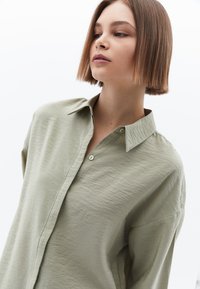 Camicia verde chiaro, strutturata, con colletto e bottoni singoli. Vestibilità ampia e design casual, senza motivi o dettagli aggiuntivi.