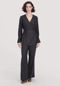 Top avvolgente nero a righe con maniche lunghe abbinato a pantaloni larghi coordinati. Strisce verticali multicolori e dettaglio della cintura in vita.