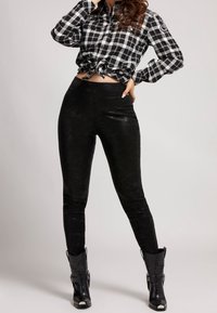 Camisa a cuadros en blanco y negro, anudada a la cintura, combinada con leggings de cuero ecológico negro de cintura alta y botas negras de tobillo.