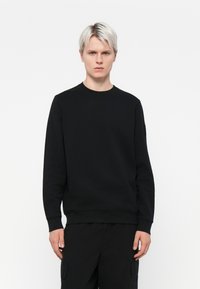 Sort sweatshirt med rund halsudskæring, lange ærmer og ribbede manchetter, lavet af et glat, struktureret stof, med en subtil detalje ved skuldersømmen.