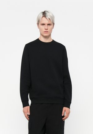 Sweat-shirt noir à col rond, manches longues et poignets côtelés, fabriqué à partir d'un tissu lisse et texturé, avec un subtil détail de couture au niveau des épaules.