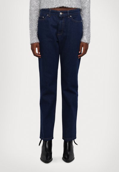 Jean en denim bleu foncé avec une taille haute, une coupe droite et des coutures discrètes. Associé à des bottines noires à talons pointus.