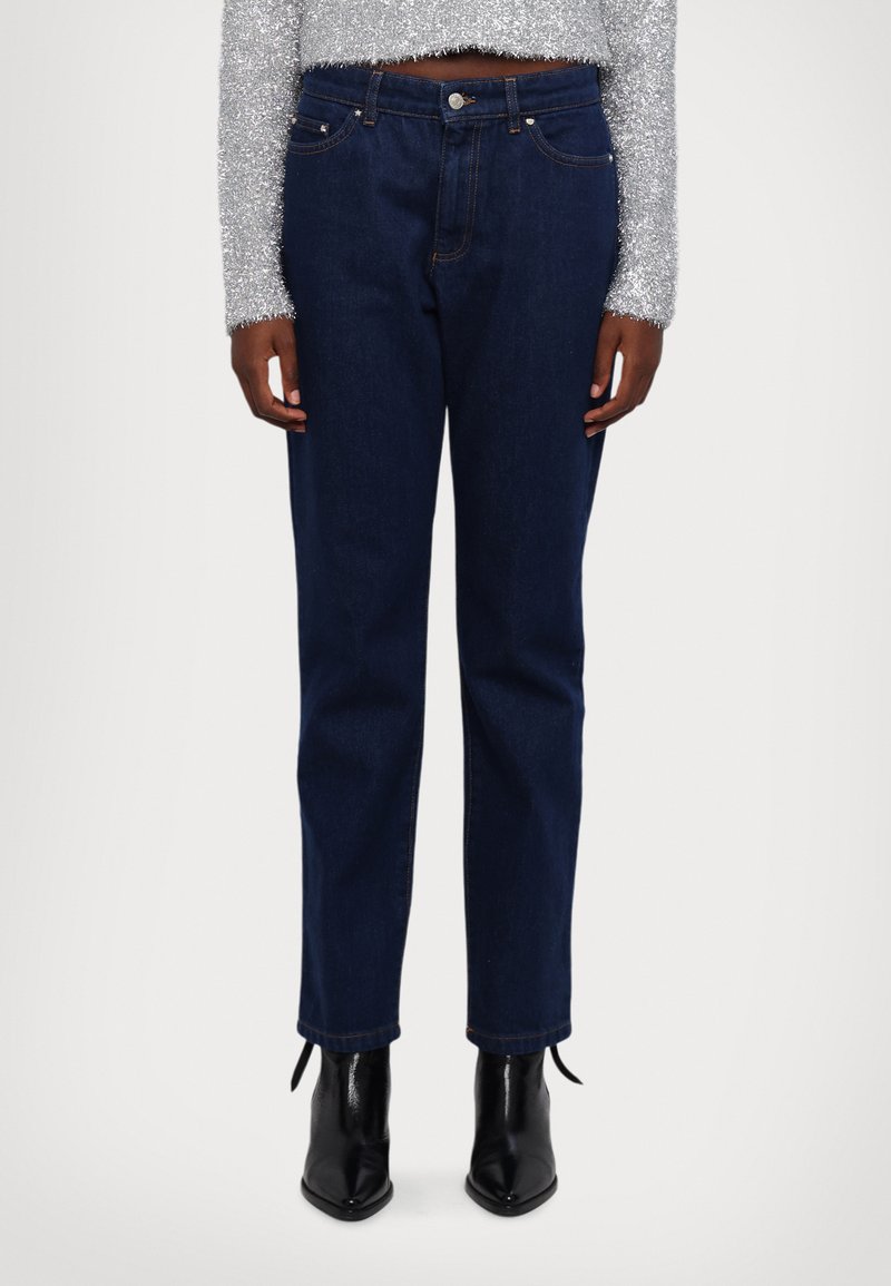 Jeans de mezclilla azul oscuro con cintura alta, diseño de pierna recta y costuras sutiles. Combinados con botas negras de tacón puntiagudo.