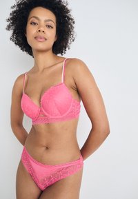 Pink lace bra with scalloped edges and thin adjustable straps, paired with matching pink lace-trimmed briefs featuring a floral pattern.