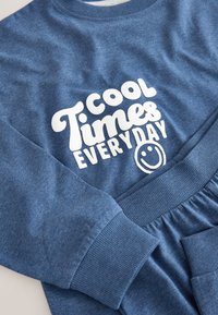 Sweat-shirt en coton bleu avec un texte blanc "cool Times EVERYDAY" et un visage souriant, avec des poignets et une ceinture côtelés. Texture douce et lisse.
