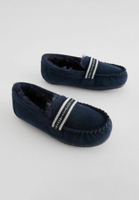 Pantofole in suede blu navy con una morbida fodera in pelliccia, dotate di una fascia a strisce in contrasto sulla parte superiore e cuciture lungo il bordo.