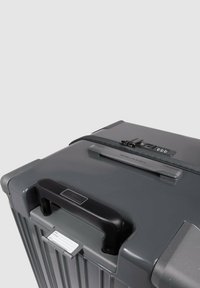 Grau Hartschalenkoffer mit strukturierter Oberfläche, vertikalen Rillen, schwarzem Griff, Zahlenschloss und einer Etikettenhalterung oben.