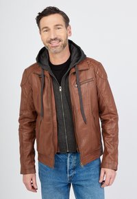 Ruskea nahkatakki, jossa on harmaa huppari sisäkerroksena, varustettuna vetoketjuilla ja taskuilla, yhdistettynä mustaan puseroon ja sinisiin farkkuihin.