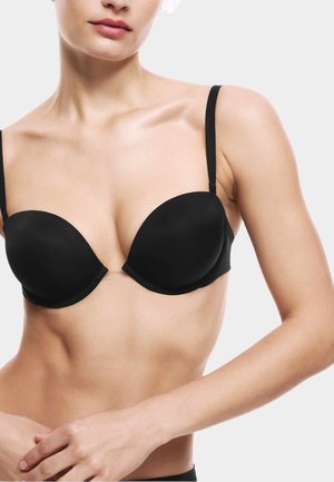 Woman wearing a black molded cup bra with thin adjustable straps against a plain white background.