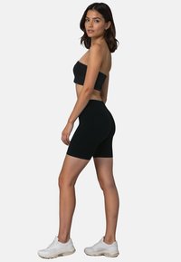 Fekete bandeau top és magas derekú kerékpáros nadrág, rugalmas anyagból. A modellen fehér sportcipők vannak. Egyszerű, testhezálló dizájn.