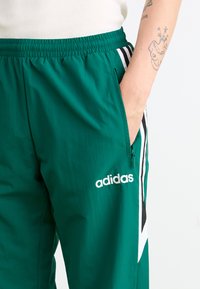 Groene Adidas sweatpants met een elastische tailleband, zijzakken en zwarte en witte strepen langs de zijkanten. Bevat geborduurd logo.
