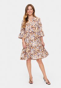 Robe maxi florale dans des tons d'orange, de bleu et de jaune, présentant un design à volants, des manches cloche et un col à boutons.