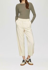 Blusa de manga larga en color verde oliva combinada con pantalones de tiro alto en color crema con bolsillos laterales y un ajuste relajado, complementada con zapatillas de estilo.