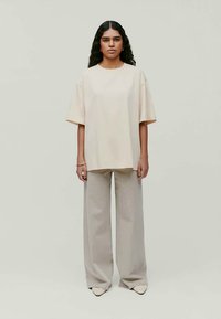 Ανοιχτό μπεζ oversize μπλούζα με κοντά μανίκια, συνδυασμένη με φαρδύ ανοιχτό γκρι παντελόνι και παπούτσια με μυτερή μύτη. Λείος υφασμάτινος χαρακτήρας σε όλη την επιφάνεια.