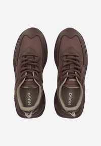 Brown fabric sneakers with a textured surface, featuring rounded toes, lace-up design, and contrasting beige accents on the tongue and interior.