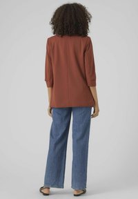 Brunröd blazer med trekvartslånga ärmar och rak skärning, kombinerad med ljusblå vida jeans och svarta sandaler.