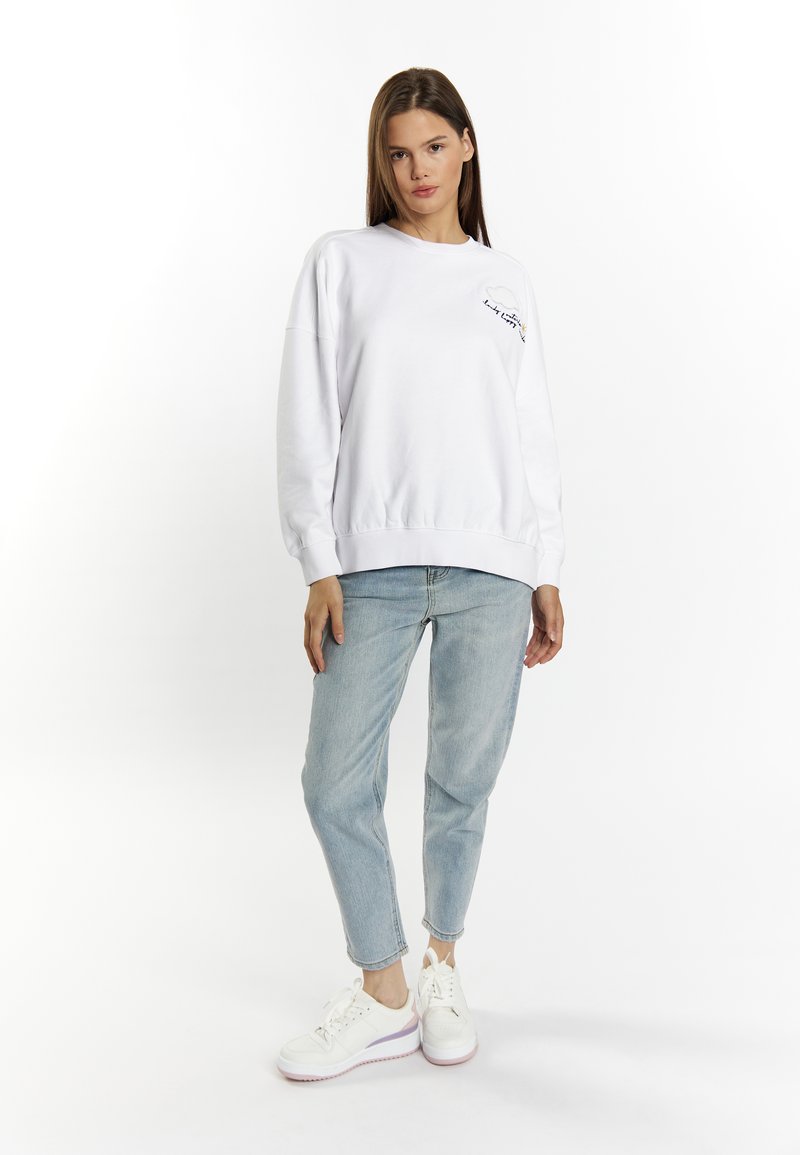 Witte sweatshirt met een ronde hals en geborduurde details, gecombineerd met lichtblauwe jeans en witte sneakers. Zachte stof, relaxte pasvorm.