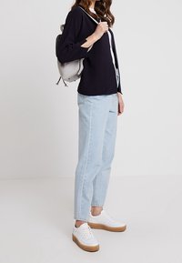 Marinblå ribbade långärmade topp, ljusblå tapered jeans, vita sneakers med gummisula och en liten ljusgrå ryggsäck.