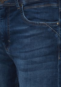 Granatowe dżinsy o gładkiej fakturze, z przednimi kieszeniami i złotymi przeszyciami wzdłuż szwów.