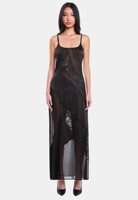 Zwarte doorschijnende maxi-jurk met spaghettibandjes, voorzien van intricat geometrische kantpatronen en een asymmetrische zoom. De stof is lichtgewicht en vloeiend.