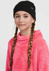 Sort strikket beanie og lyserød fuzzy pullover med høj krave, en luksuriøs tekstur og lange fletninger, der indrammer ansigtet.