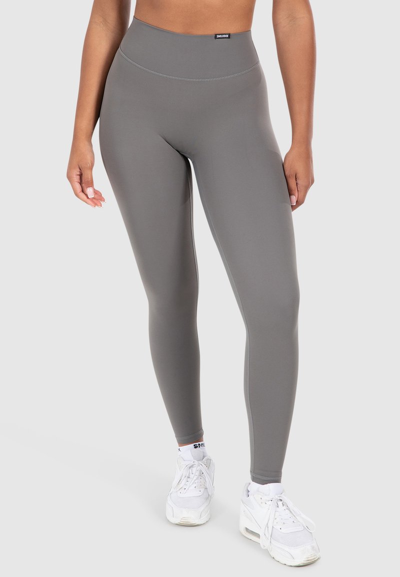 Leggings grigi in tessuto elastico, con una vita alta e una superficie liscia. Abbinati a scarpe sportive bianche.
