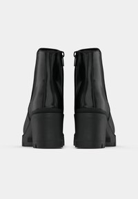 Svarta ankelboots med en slät, glansig yta, utrustade med en klumpig klack och bakre dragkedjor. Designen är enkel och slimmad utan synliga mönster.