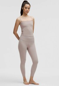Jasnoróżowy top na ramiączkach z cienkimi szelkami, zestawiony z dopasowanymi leggingsami o wysokim stanie. Oba elementy wykonane są z miękkiego, elastycznego materiału.