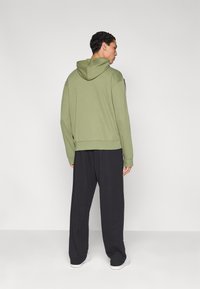 Sweat à capuche vert olive avec capuche, poignets et ourlet côtelés, associé à un pantalon noir ample. Design simple et minimaliste.