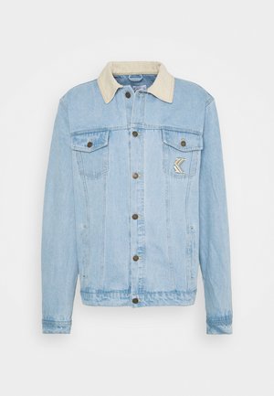 Veste en jean bleu clair avec col beige, fermetures par boutons, deux poches poitrine et un patch logo chevron sur la poche poitrine gauche.